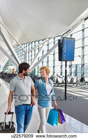 Stock Photo - Portrait of mature couple walking while talking in airport. Fotosearch