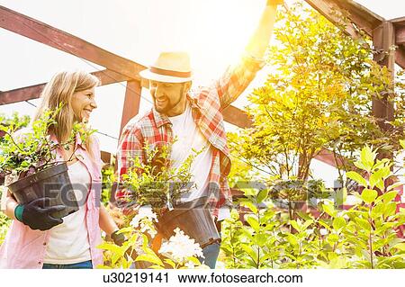 Stock Image - Portrait of mature female and male gardeners carrying plants on pot . Fotosearch