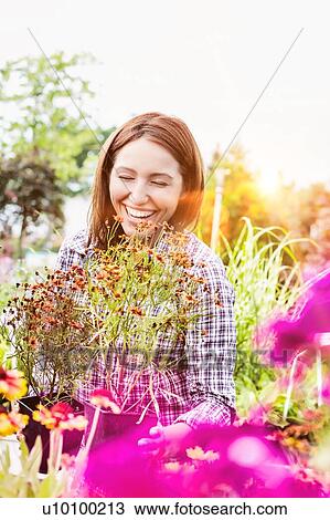 Stock Image - Portrait of mature female gardener arranging flowers on pot in shop. Fotosearch