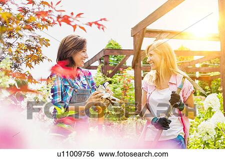 Portrait of mature female gardeners standing while talking View Large Photo Image Stock Photograph - Portrait of mature female gardeners standing while talking . Fotosearch