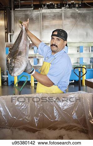 Stock Image - Portrait of mature fishmonger holding salmon fish. Fotosearch