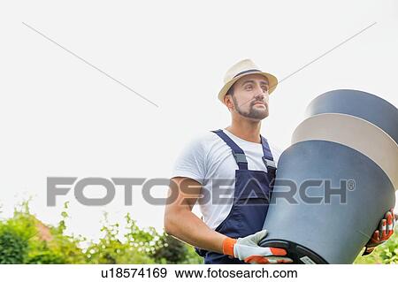 Stock Photo - Portrait of mature gardener carrying pots in shop. Fotosearch