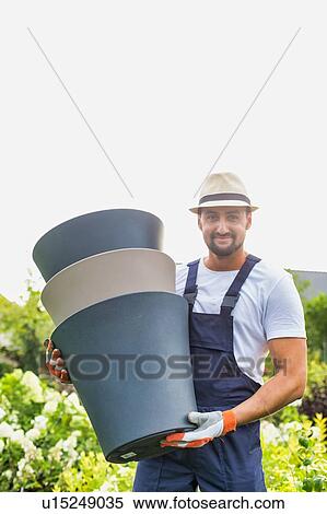 Stock Photography - Portrait of mature gardener carrying pots in shop. Fotosearch