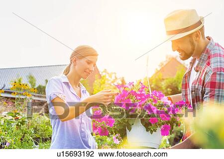Stock Image - Portrait of mature gardener showing woman buyer flowers on pot in shop. Fotosearch