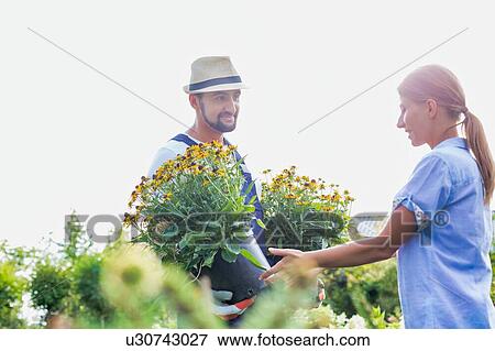 Stock Photo - Portrait of mature gardener showing flowers to woman buyer in shop. Fotosearch