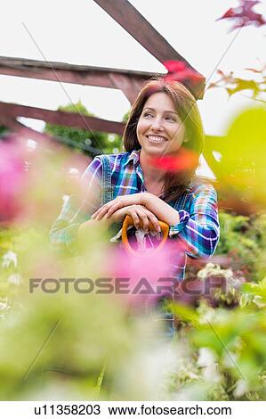 Stock Image - Portrait of mature gardener smiling while leaning on shovel . Fotosearch