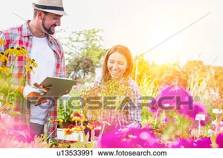 Portrait of mature gardener writing report on clipboard while female gardener arranging flowers on pot View Large Photo Image Stock Image - Portrait of mature gardener writing report on clipboard while female gardener arranging flowers on pot. Fotosearch