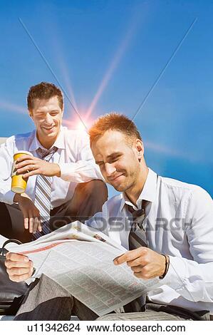 Picture - Portrait of mature handsome businessman reading newspaper against collegue during break. Fotosearch