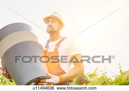 Stock Photograph - Portrait of mature male gardener carrying pots in shop. Fotosearch