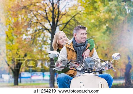 Stock Photo - Portrait of mature man driving motorbike with his wife in park. Fotosearch