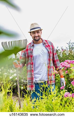 Stock Photography - Portrait of mature man holding fork rake in garden shop. Fotosearch