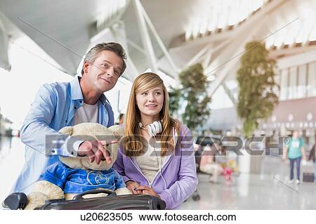 Stock Photography - Portrait of mature man pushing baggage cart while walking with her daughter in airport with lens flare. Fotosearch