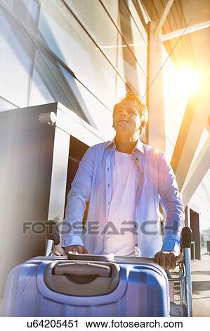 Stock Image - Portrait of mature man pushing cart with his suitcase in airport. Fotosearch