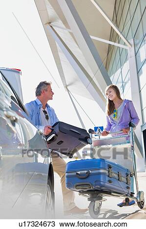 Stock Image - Portrait of mature man putting luggage on car trunk with lens flare. Fotosearch