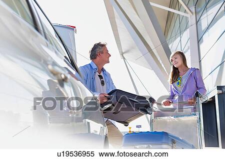 Stock Photography - Portrait of mature man putting luggage on car trunk with lens flare. Fotosearch