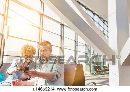 Picture - Portrait of mature man showing smartphone to his wife while waiting for their flight in airport. Fotosearch