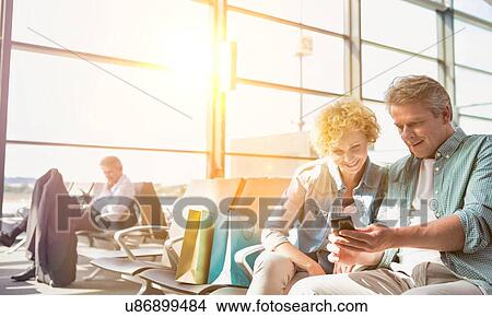 Picture - Portrait of mature man showing smartphone to his wife while waiting for their flight in airport. Fotosearch