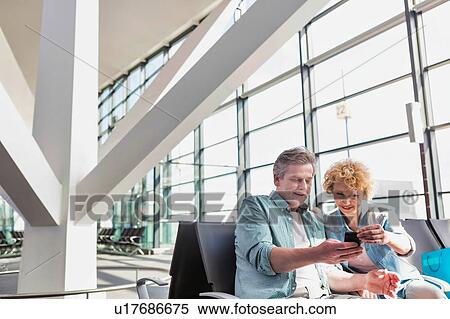 Stock Photography - Portrait of mature man showing smartphone to his wife while waiting for their flight in airport. Fotosearch