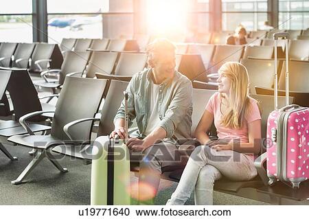 Stock Image - Portrait of mature man talking to her daughter while waiting and sitting in airport with yellow lens flare. Fotosearch