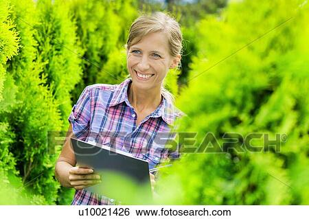 Portrait of mature owner smiling while writing report on clipboard in garden View Large Photo Image Stock Photograph - Portrait of mature owner smiling while writing report on clipboard in garden . Fotosearch