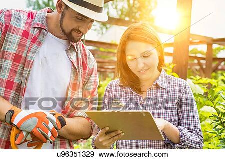 Portrait of mature owner writing report on clipboard with the gardener in shop View Large Photo Image Stock Photo - Portrait of mature owner writing report on clipboard with the gardener in shop. Fotosearch