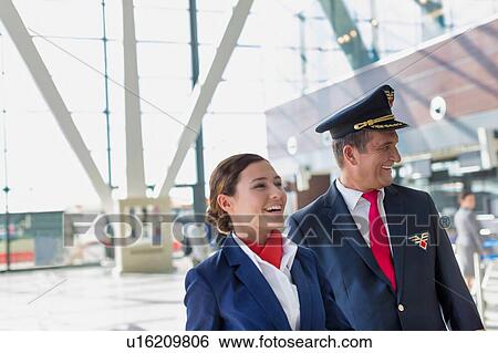Stock Photograph - Portrait of mature pilot and attractive flight attendant walking while smiling in airport. Fotosearch
