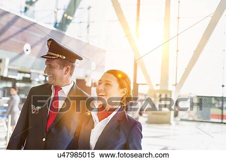 Stock Photography - Portrait of mature pilot and attractive flight attendant walking while smiling in airport. Fotosearch