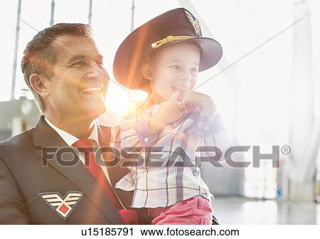 Stock Image - Portrait of mature pilot carrying cute little child in airport. Fotosearch
