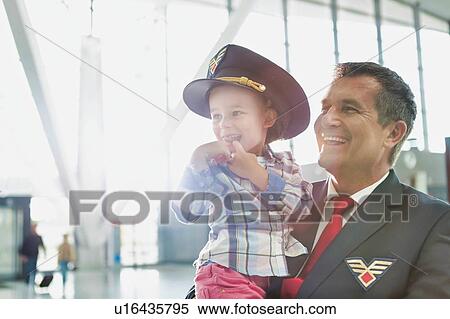 Stock Photography - Portrait of mature pilot carrying cute little child in airport. Fotosearch