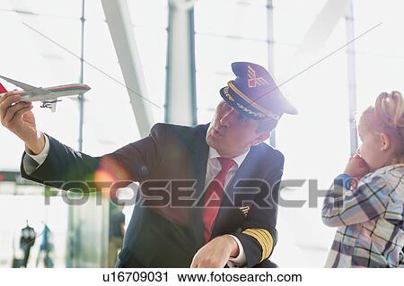 Portrait of mature pilot holding airplane toy while playing with cute little girl in airport View Large Photo Image Stock Image - Portrait of mature pilot holding airplane toy while playing with cute little girl in airport. Fotosearch