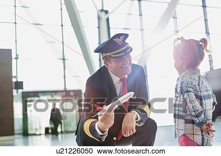Stock Image - Portrait of mature pilot holding airplane toy while playing with cute little girl in airport. Fotosearch