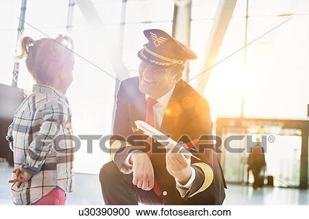 Stock Image - Portrait of mature pilot holding airplane toy while playing with cute little girl in airport. Fotosearch