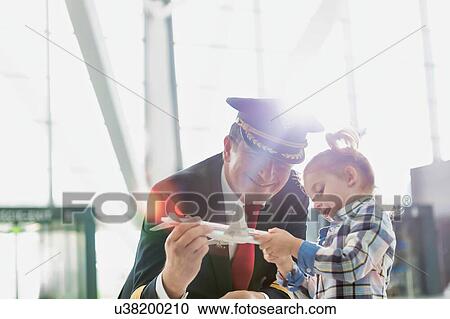 Stock Image - Portrait of mature pilot holding airplane toy while playing with cute little girl in airport. Fotosearch