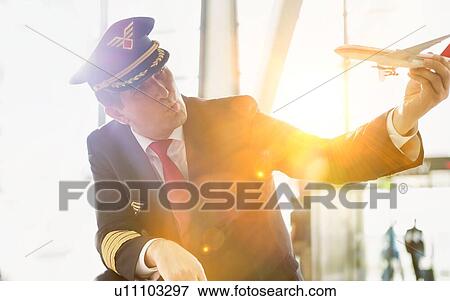 Stock Photo - Portrait of mature pilot holding airplane toy while playing with cute little girl in airport. Fotosearch