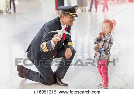 Stock Photography - Portrait of mature pilot holding airplane toy while playing with cute little girl in airport. Fotosearch