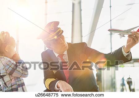 Stock Photography - Portrait of mature pilot holding airplane toy while playing with cute little girl in airport. Fotosearch