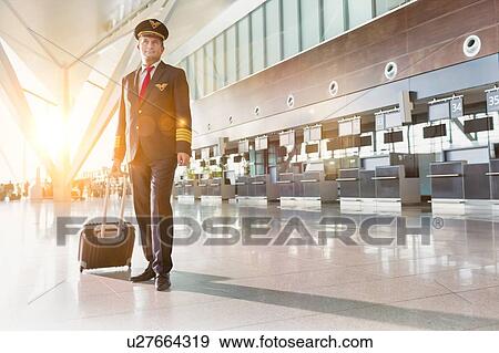 Stock Photo - Portrait of mature pilot standing in check in area at airport . Fotosearch