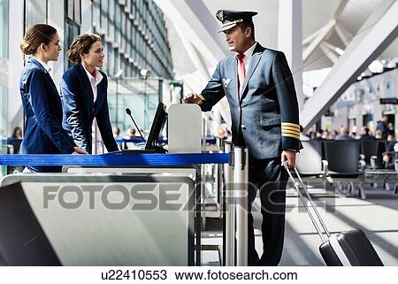 Stock Image - Portrait of mature pilot talking with the airport staffs in boarding gate. Fotosearch