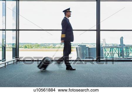 Picture - Portrait of mature pilot walking in airport with yellow lens flare . Fotosearch