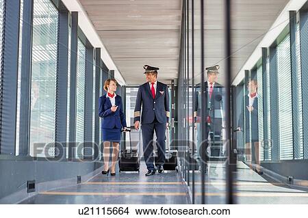 Picture - Portrait of mature pilot walking with young attractive stewardess in airport. Fotosearch