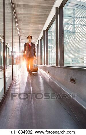 Stock Image - Portrait of mature pilot walking with his suitcase in airport. Fotosearch