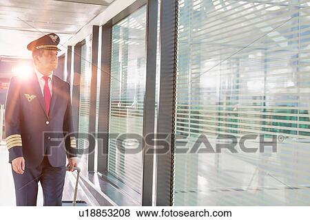 Stock Photo - Portrait of mature pilot walking with his suitcase in airport. Fotosearch