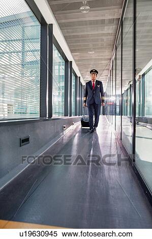 Stock Photography - Portrait of mature pilot walking with his suitcase in airport. Fotosearch