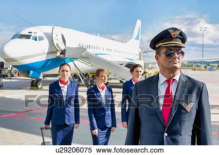 Portrait of mature pilot walking with three young beautiful flight attendants against airplane in airport View Large Photo Image Stock Photography - Portrait of mature pilot walking with three young beautiful flight attendants against airplane in airport. Fotosearch