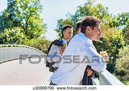 Portrait of mature thoughtful attractive businessman drinking coffee while standing on the bridge with colleagues View Large Photo Image Stock Image - Portrait of mature thoughtful attractive businessman drinking coffee while standing on the bridge with colleagues . Fotosearch