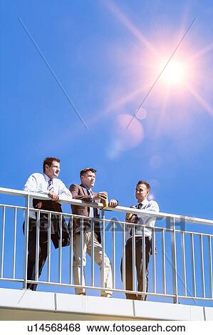 Stock Photo - Portrait of mature thoughtful attractive businessman drinking coffee while standing on the bridge with colleagues . Fotosearch