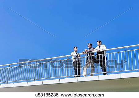 Stock Photograph - Portrait of mature thoughtful attractive businessman drinking coffee while standing on the bridge with colleagues . Fotosearch