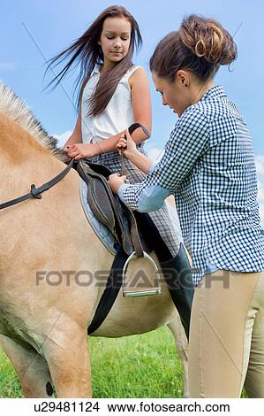Picture - Portrait of mature woman adjusting leathers on horse for stirrup iron in ranch. Fotosearch