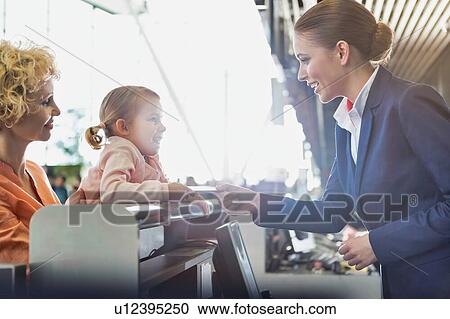 Stock Image - Portrait of mature woman carrying her cute little child while she is giving her passport with lens flare in airport. Fotosearch