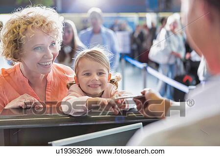Stock Photograph - Portrait of mature woman carrying her cute little child while she is giving her passport with lens flare in airport. Fotosearch
